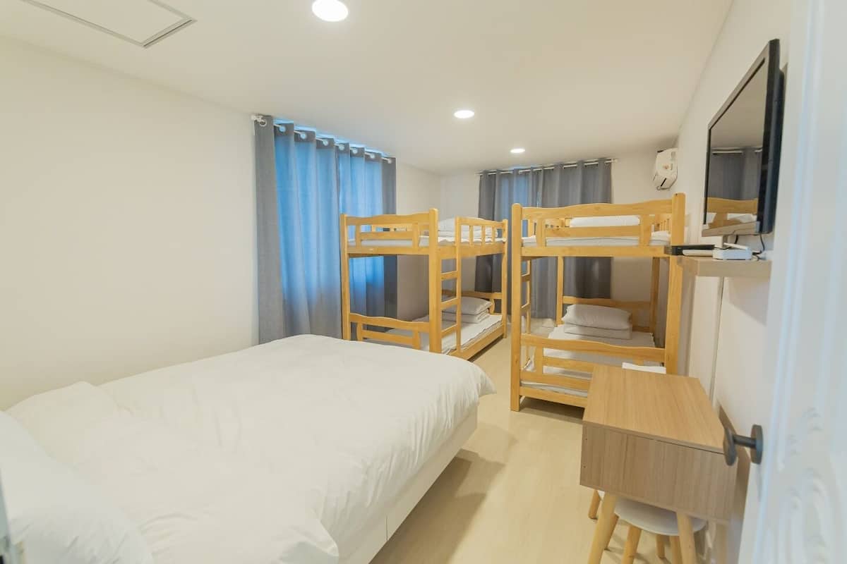 Una habitación con literas, un escritorio, una silla, una cama y un televisor en la pared.