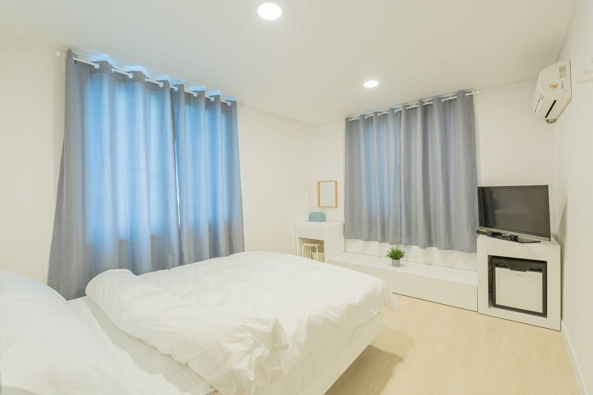 Habitación de hotel con dos camas, un televisor, un escritorio pequeño y una planta.