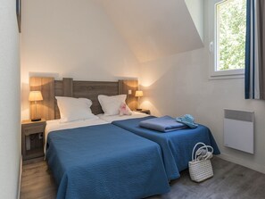 Ein Schlafzimmer mit zwei Betten, Nachttischlampen, einem Fenster mit Vorhängen und einer Heizung.