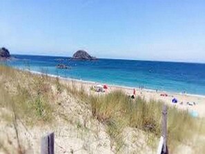 Ein Strand mit blauem Himmel, sandigem Ufer und einer kleinen Insel in der Ferne.