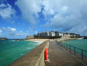 A coastal promenade with a historic building, a sandy beach, and the sea.
