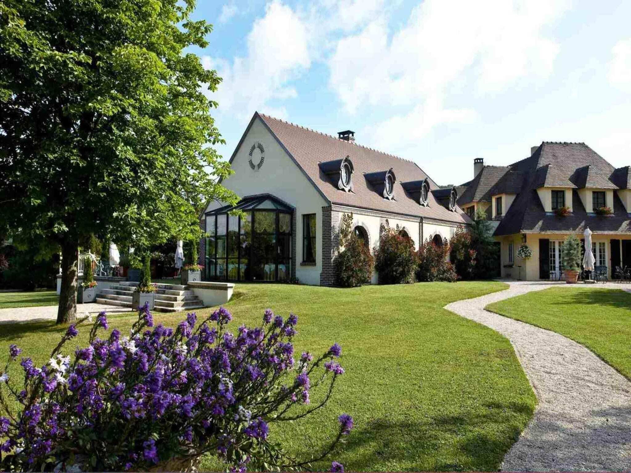A large, two-story building with a symmetrical facade, a central entrance with steps, and a well-maintained lawn with purple flowers.