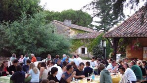 A group of people dining outdoors at a rustic setting with stone buildings and greenery in the background.