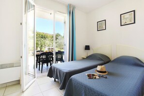 Ein Hotelzimmer mit zwei Betten, einer Essecke mit Stühlen und Blick auf Grünflächen.