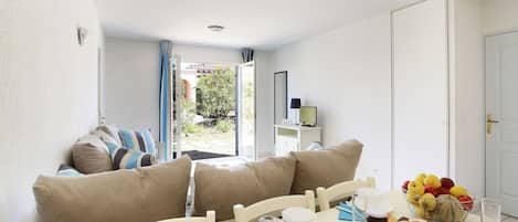 Una habitación con una mesa de comedor lista para el desayuno, un sofá con cojines, una ventana con cortinas y una puerta.