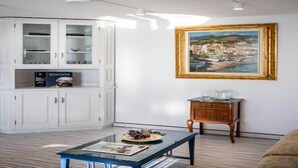 A living room with a glass-top coffee table, a white cabinet with glass doors, a framed painting on the wall, and a small wooden side table. - Chic Hideaway in Positano (Positano)