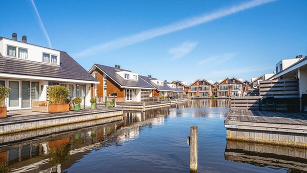 A canal-side residential area with houses on both sides, a wooden dock, and calm water reflecting the buildings. - Apartment in Egmond with Stunning Sea Views (Egmond aan zee)