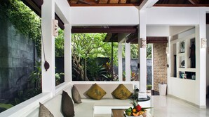 A modern living room with a white sofa, a wooden coffee table with fruit, and a view of lush greenery outside. - Villa Teman (Buleleng)