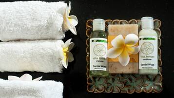 Three white towels, two bottles of 'villa teman shampoo' and 'villa teman conditioner', and a bar of soap on a decorative tray.