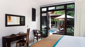 A hotel room with a bed, a desk, a chair, and a view of an outdoor pool area. - Villa Teman (Buleleng)