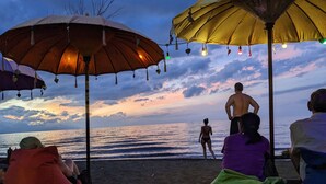 A beach scene with people sitting under umbrellas, overlooking the ocean. - Villa Teman (Buleleng)