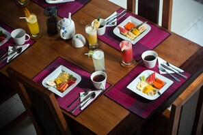 A dining table set with plates of fruit, a coffee pot, a teapot, and various beverages. - Villa Teman (Buleleng)