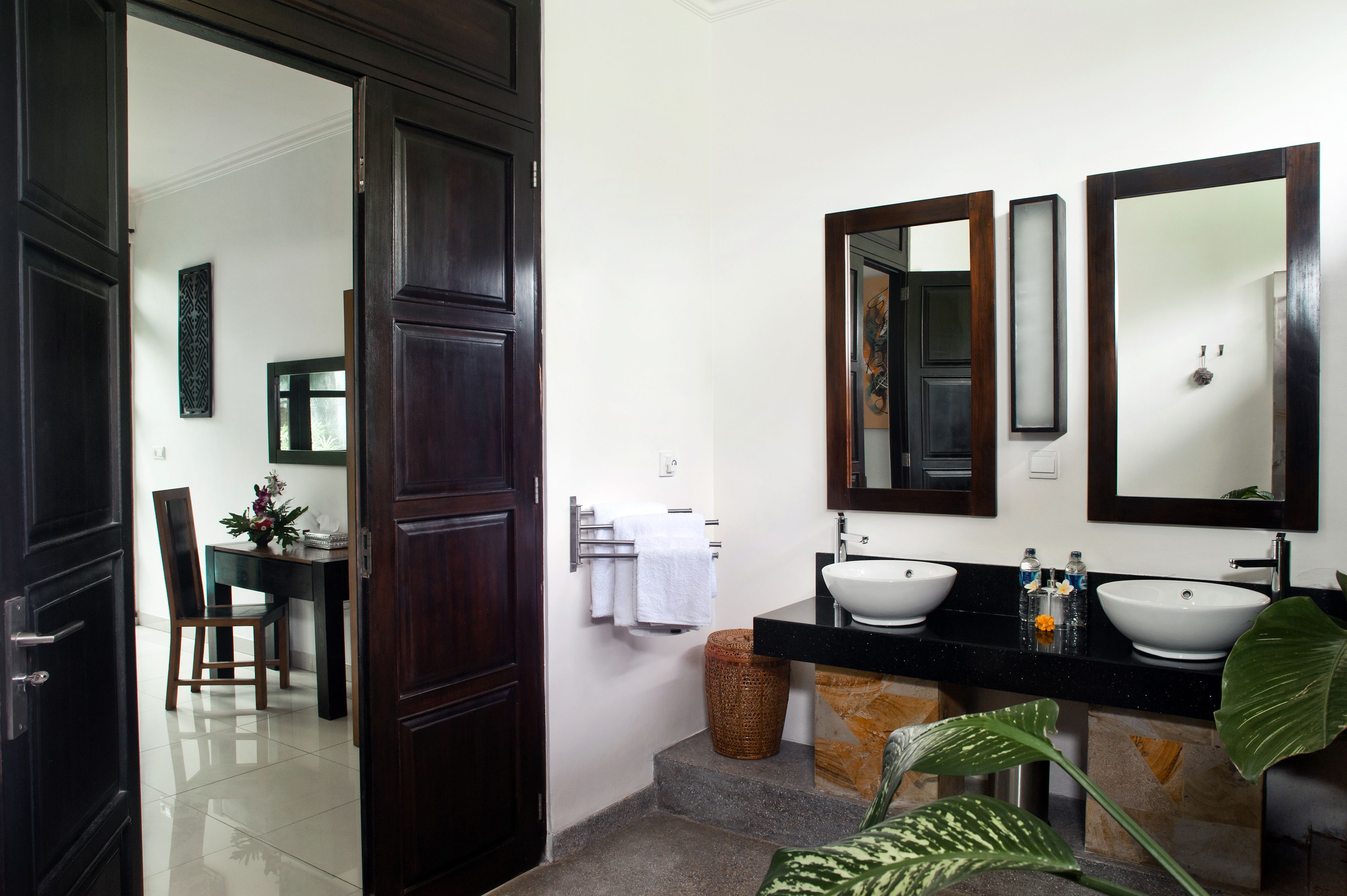 A bathroom with two sinks, a mirror, and a door leading to a dining area.