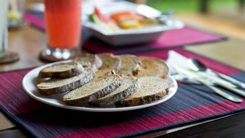 Ein Teller mit Brotscheiben auf einer Unterlage, dazu ein Glas rotes Getränk und im Hintergrund eine Obstplatte.