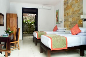 A hotel room with two beds, a desk, and a chair. There is a stone wall and a door leading to an outdoor area. - Villa Teman (Buleleng)