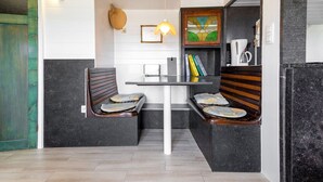 A small, cozy seating area with two wooden benches and a table, a wall-mounted light fixture, and a framed artwork.
