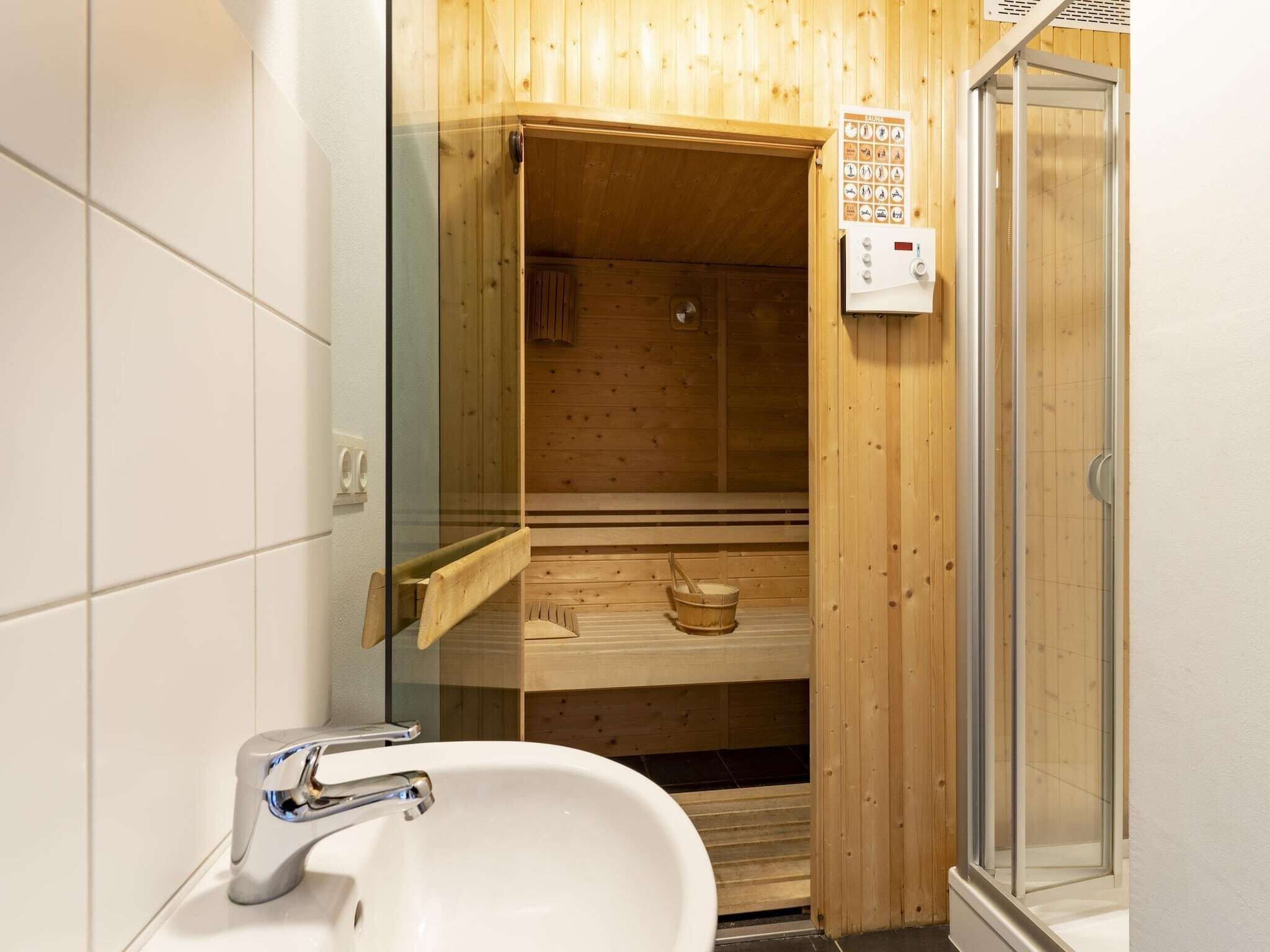 Ein Saunaraum aus Holz mit Glastür, einer Holzbänke, einem Holz-Eimer und einer Steuerung.