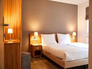 Ein Hotelzimmer mit einem hölzernen Kopfteil, zwei Nachttischlampen, einem Bett mit weißer Bettwäsche und einem kleinen Holznachttisch.