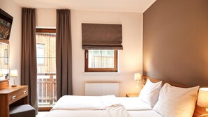 Ein Hotelzimmer mit zwei Betten, einem Fenster mit Aussicht, einem Heizkörper und einer Nachttischkommode mit Lampe.