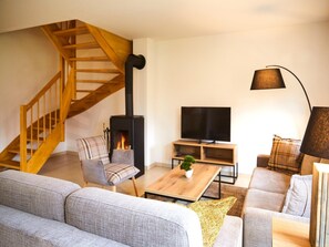 Un salon avec un escalier en bois, une cheminée, un téléviseur et un canapé.