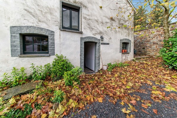 A white building with a stone wall, a paved driveway, and a small garden area with fallen leaves.