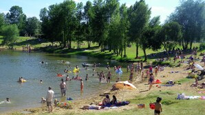 Un parque concurrido junto al lago, con gente nadando, tomando el sol y paseando por la orilla.