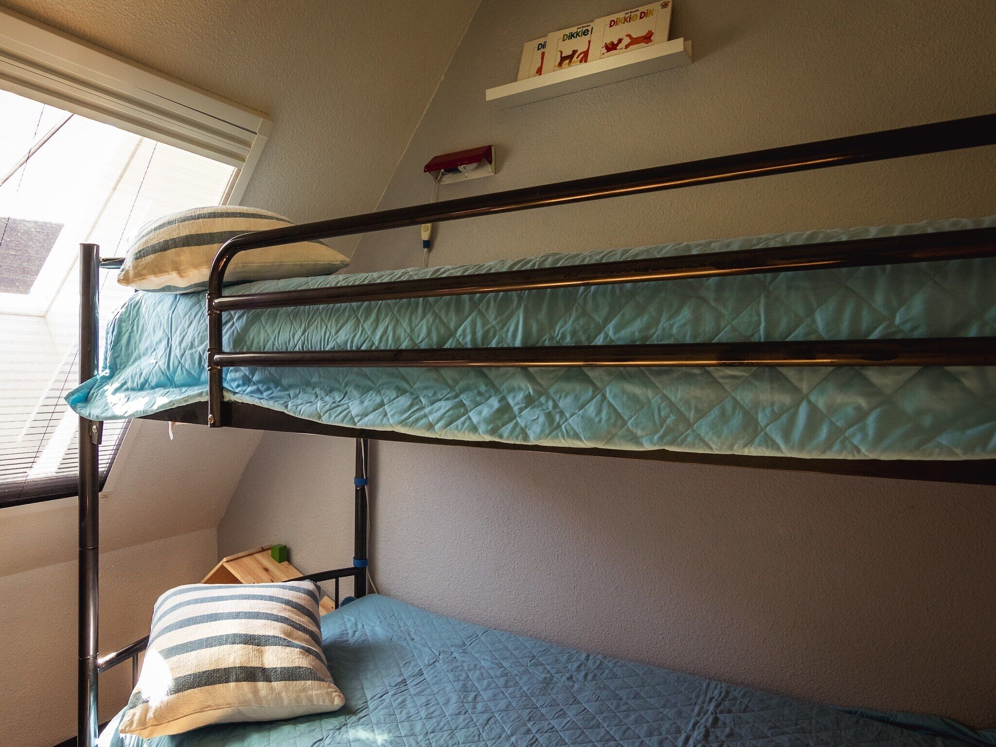 A bunk bed with a quilted mattress, a striped pillow, and a shelf with books.