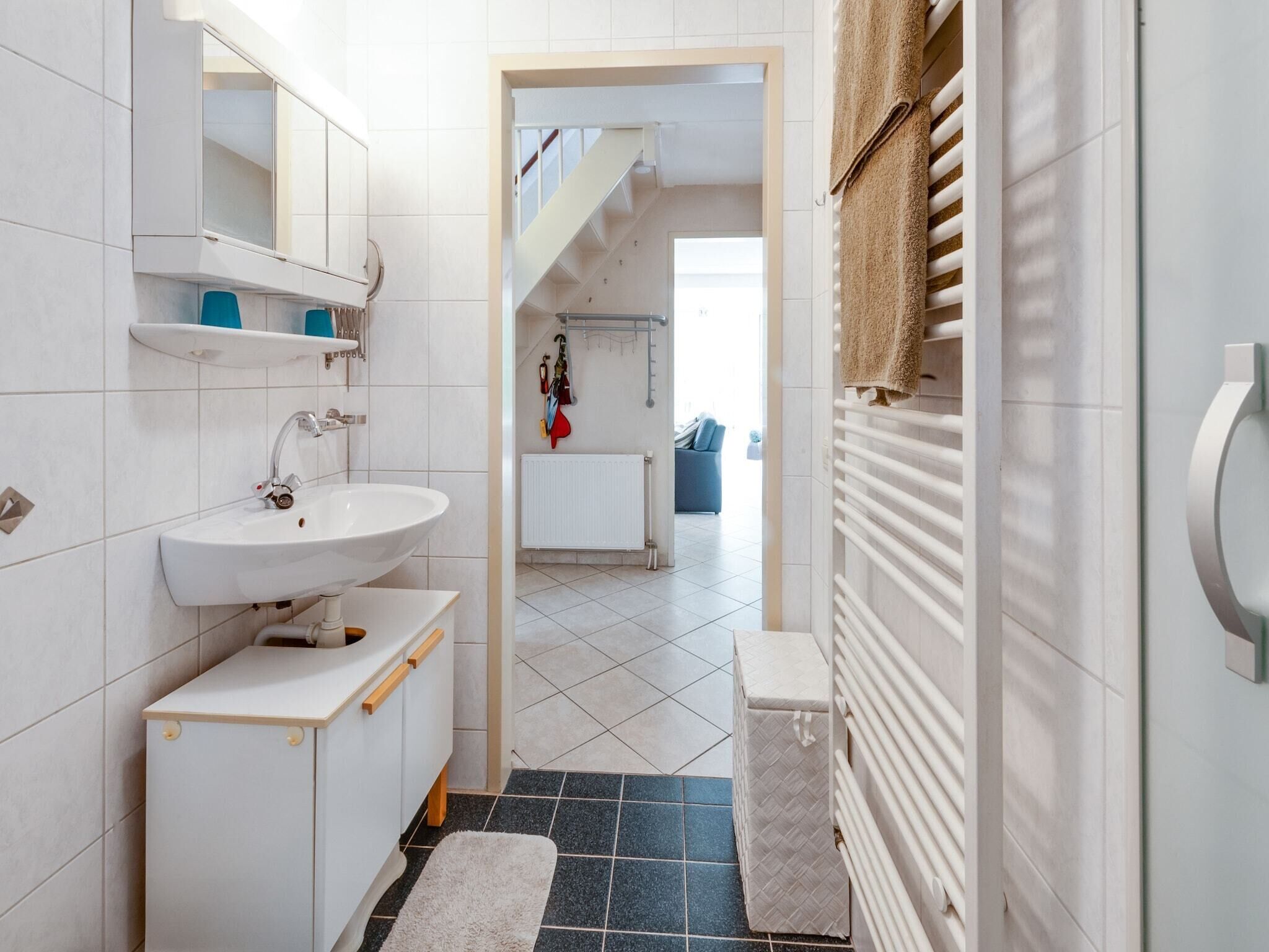 A modern bathroom with a white sink, mirror, and towel rack. A staircase leads to a living area with a blue sofa.