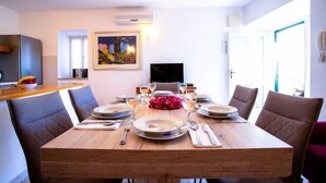 A dining area with a wooden table set for four, surrounded by cushioned chairs. A painting is on the wall, and a flat-screen TV is mounted above the table. - Villa in Sumartin near Beach & Private Pool (Sumartin)