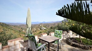 A patio with a table and chairs, a green umbrella, and a view of a hilly landscape. - Villa Mariposa in Spain's Sunny Paradise (Arenas)