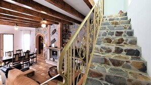 A spacious living area with a stone fireplace, wooden beams, and a staircase with a wrought iron railing. - Villa Mariposa in Spain's Sunny Paradise (Arenas)
