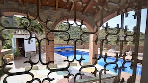 A pool area with a view of a mountainous landscape, a small building, and a covered seating area with a decorative metal fence. - Villa Mariposa in Spain's Sunny Paradise (Arenas)