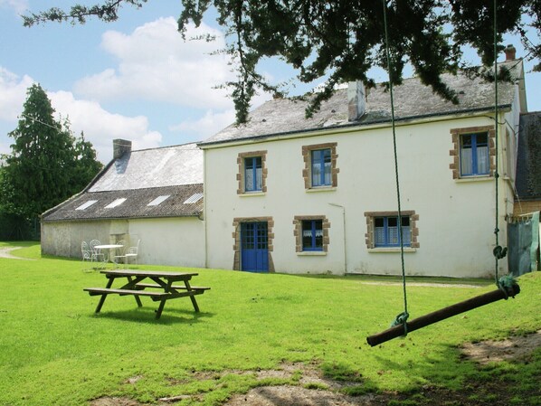 A building with a picnic table and swing set in a grassy area.