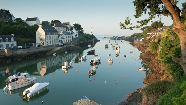 A harbor with boats, a lighthouse, and buildings along the shore. - Wildlife Haven Near Le Pouldu (Clohars-Carnoet)