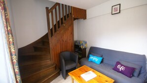 A living room with a wooden staircase, a grey sofa with two cushions, a wooden coffee table, and a small bookshelf. - Wildlife Haven Near Le Pouldu (Clohars-Carnoet)