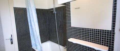Un baño con ducha, lavamanos y espejo.
