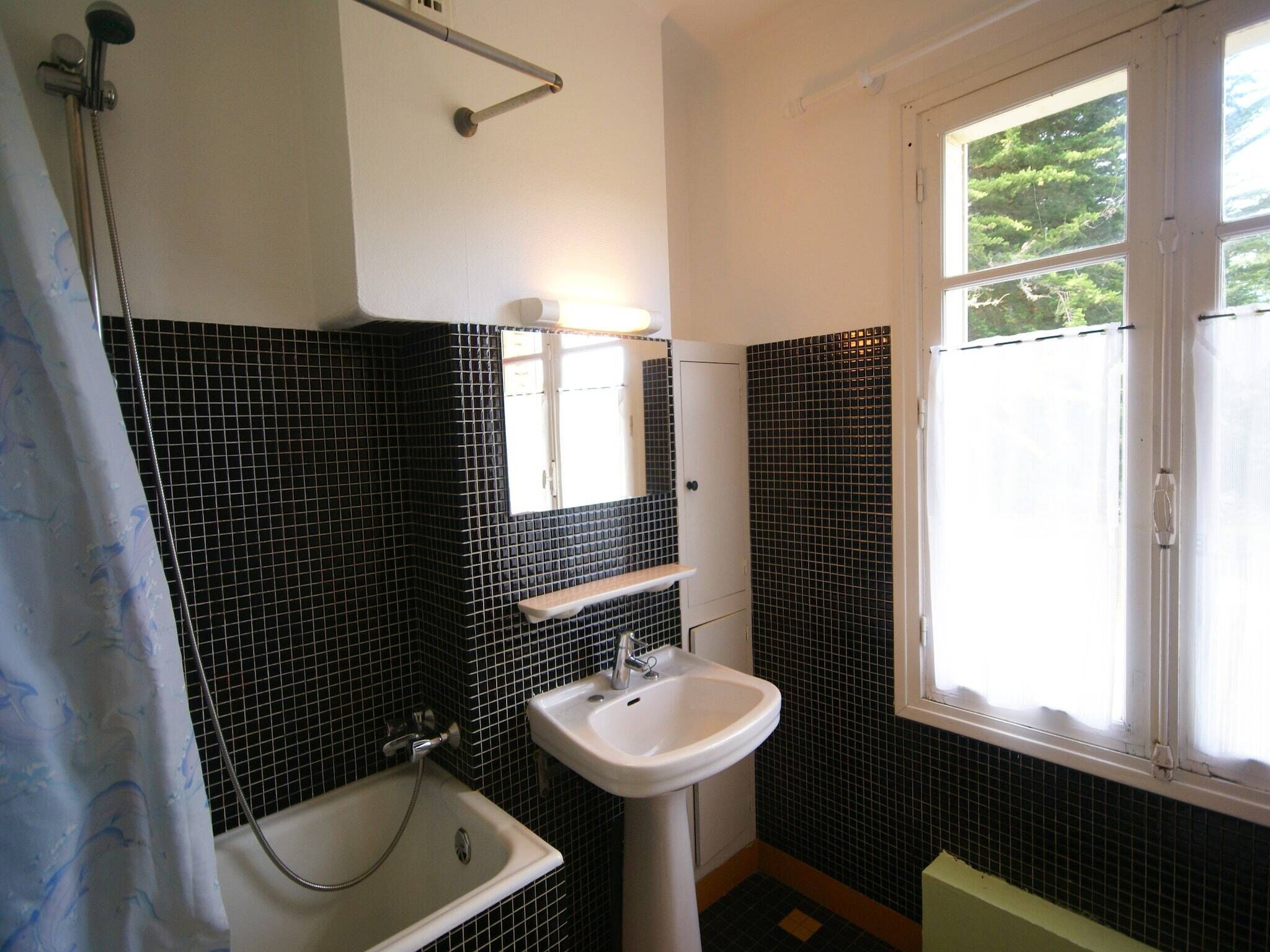 Un baño con bañera, lavabo, ventana y paredes con baldosas blanco y negro.