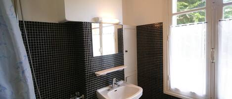 Un baño con bañera, lavabo, ventana y paredes con baldosas blanco y negro.