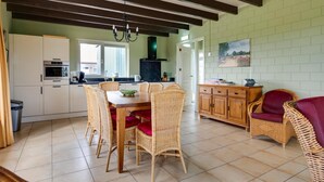 A kitchen with white cabinets, a dining table with wicker chairs, and a red sofa. - Holiday Home Schoonoord near Kibbelkoele (Kibbelveen)
