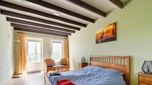 A bedroom with a wooden bed, checkered bedding, a painting, a nightstand, a chair, and a window with curtains. - Holiday Home Schoonoord near Kibbelkoele (Kibbelveen)