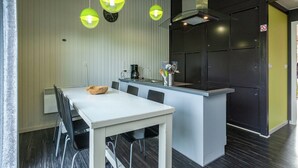 Eine moderne Küche mit einem weißen Tisch und Stühlen, einer schwarzen Arbeitsplatte und grünen Pendelleuchten.