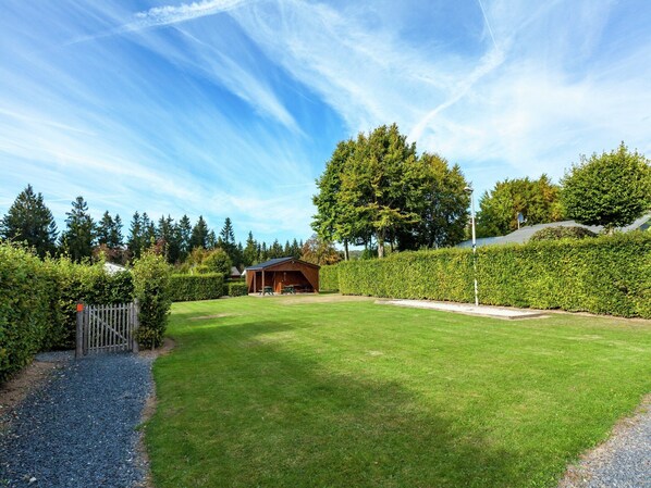 A well-maintained lawn with a wooden structure, likely a gazebo, surrounded by a hedge and trees.