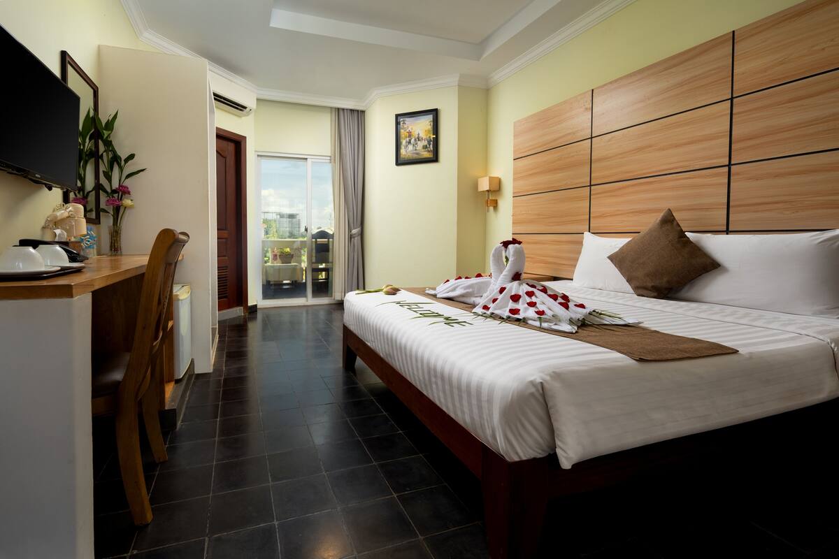 A hotel room with a bed, a desk, a chair, a TV, and a balcony with a view.
