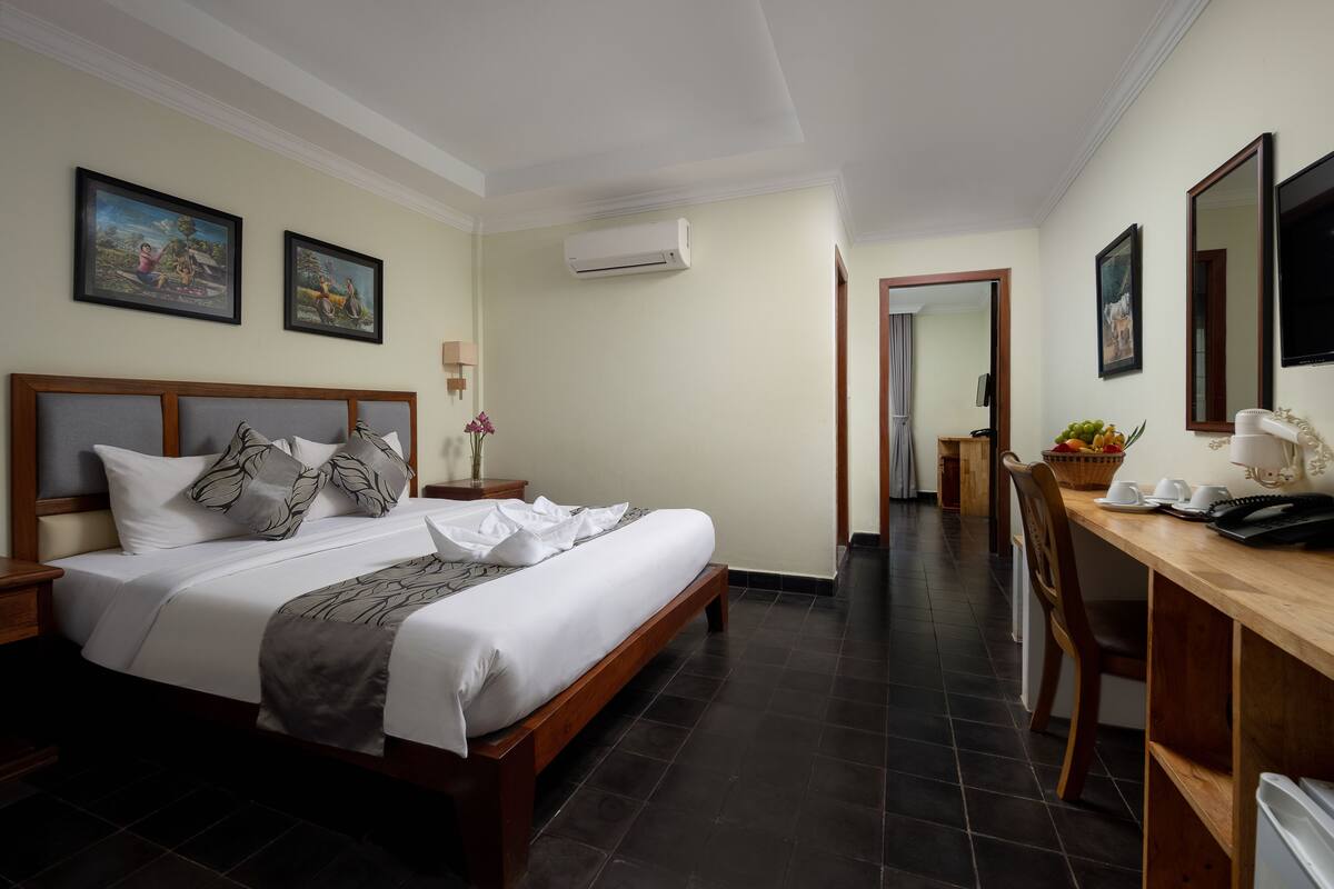 A hotel room with a large bed, a desk with a chair, a television, and artwork on the walls.