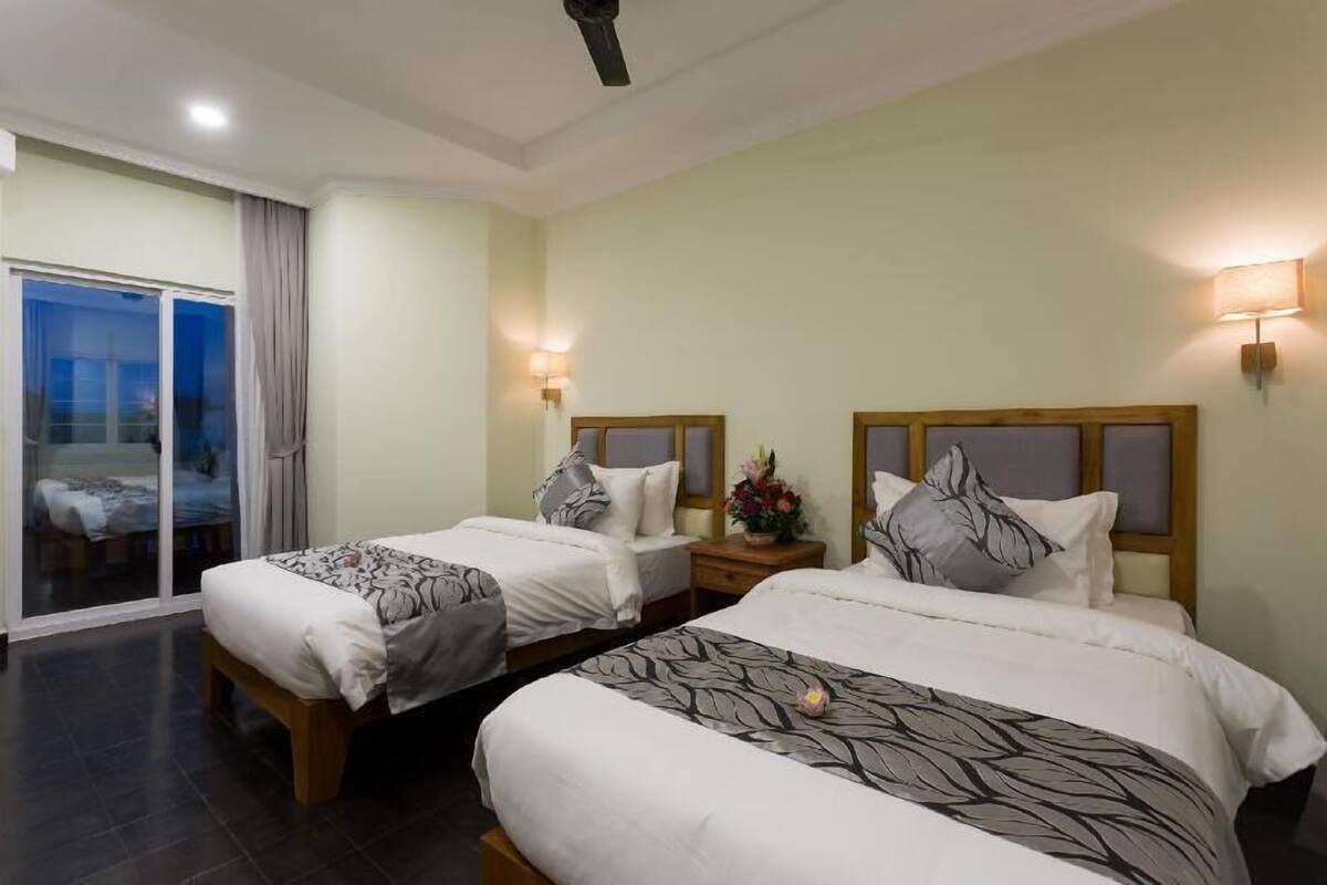 A hotel room with two beds, a sliding glass door to a balcony, and a ceiling fan.