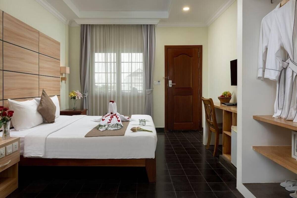 A hotel room with a bed, a wooden headboard, a desk, a chair, a wardrobe, and a door.