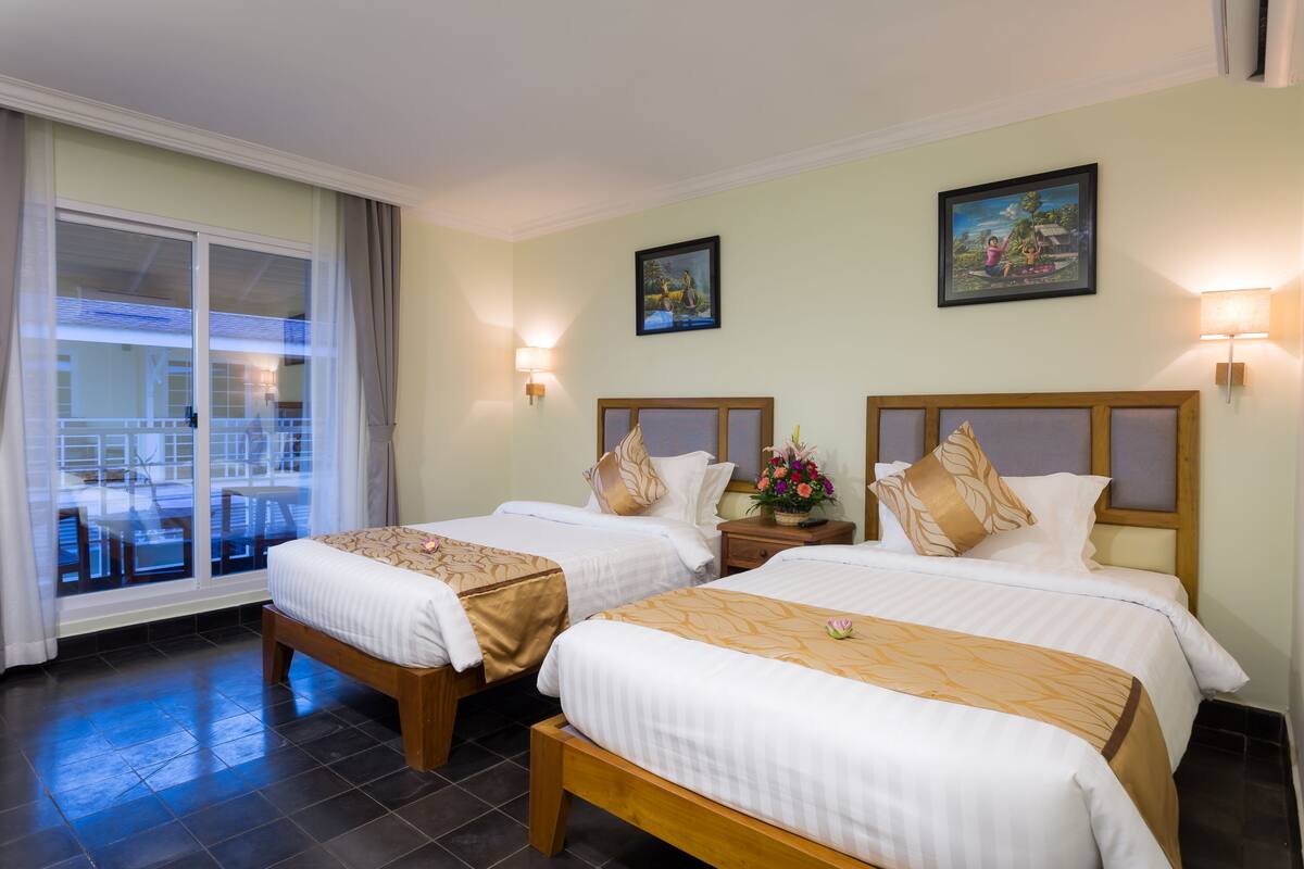 A hotel room with two beds, a balcony with a view, and a painting on the wall.