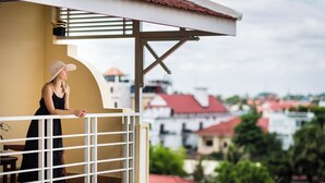A balcony with a railing, a person leaning on it, and a view of buildings in the background. - Grand Bayon Siem Reap Hotel (Siem Reap)