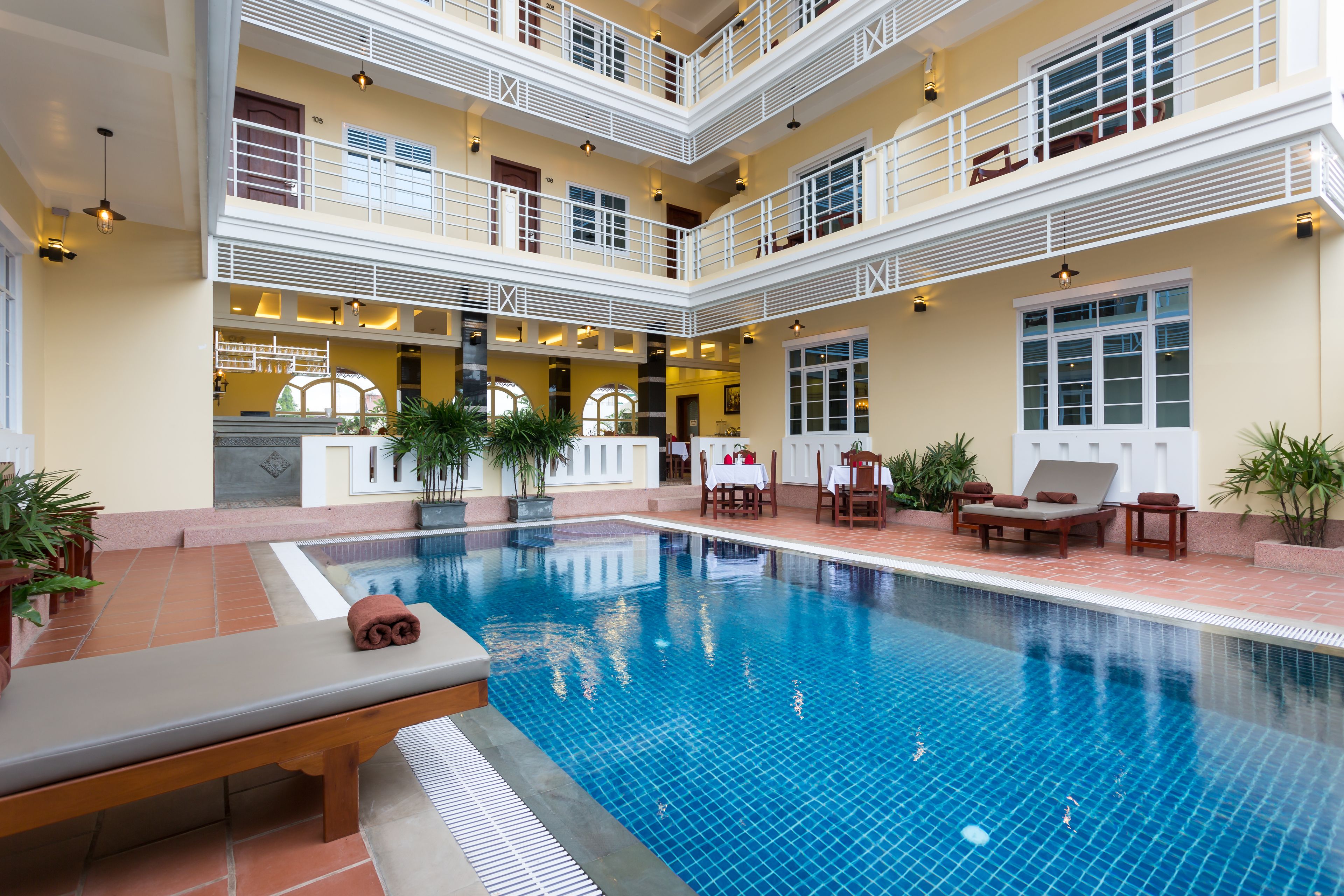A multi-level indoor swimming pool with lounge areas, potted plants, and a reception desk.