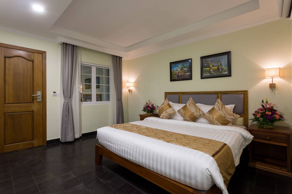 A hotel room with a large bed, two bedside tables with lamps, a wooden door, and a window with curtains.